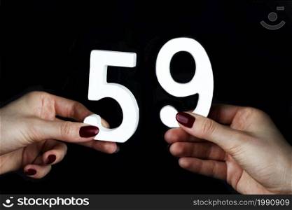 On a black background, female hand with number fifty-nine.. On the female palms figure fifty-nine.