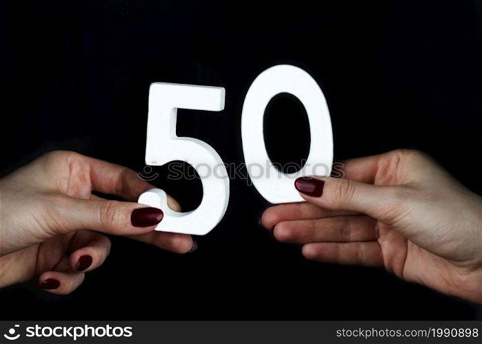 On a black background, female hand with number fifty.. On the female palms figure fifty.