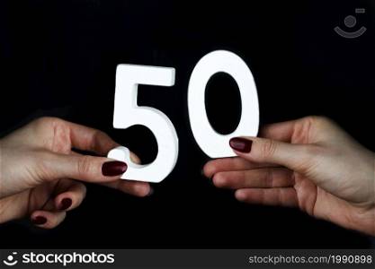 On a black background, female hand with number fifty.. On the female palms figure fifty.