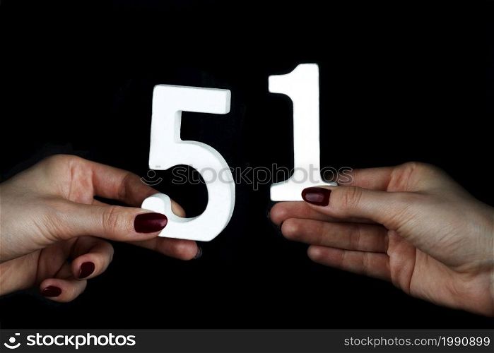 On a black background, female hand with number fifty-one.. On the female palms figure fifty-one.
