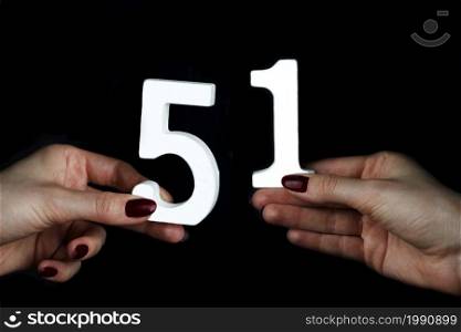 On a black background, female hand with number fifty-one.. On the female palms figure fifty-one.