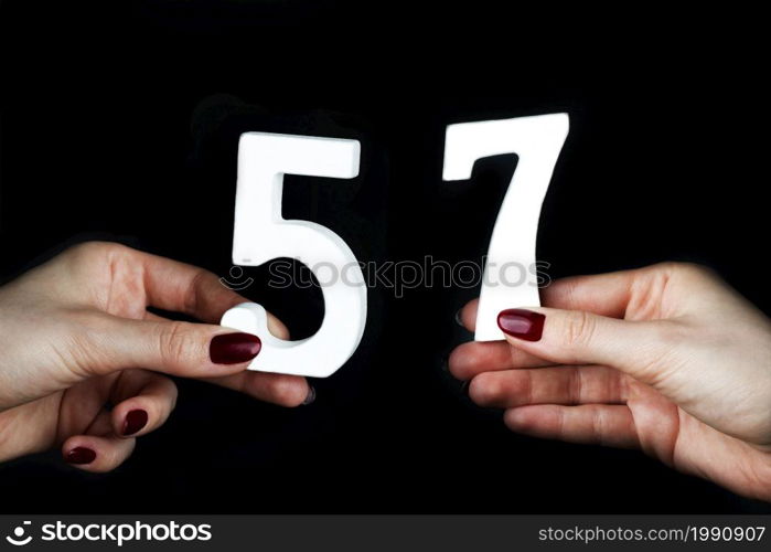On a black background, female hand with number fifty-seven.. On the female palms figure fifty-seven.
