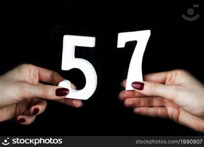 On a black background, female hand with number fifty-seven.. On the female palms figure fifty-seven.