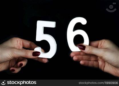 On a black background, female hand with number fifty-six.. To female hands the number fifty-six.