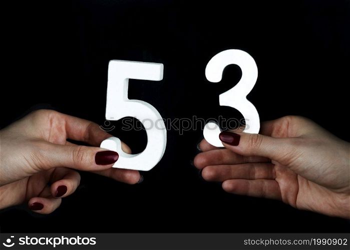On a black background, female hand with number fifty-three.. On the female palms figure fifty-three.