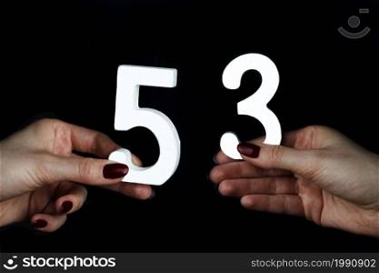 On a black background, female hand with number fifty-three.. On the female palms figure fifty-three.