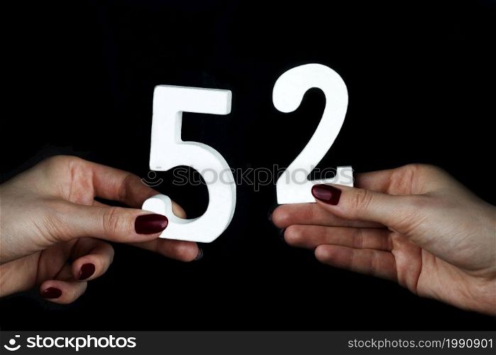 On a black background, female hand with number fifty-two.. On the female palms figure fifty-two.