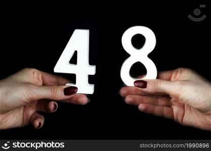 On a black background, female hand with number forty-eight.. To female hands the number forty-eight.