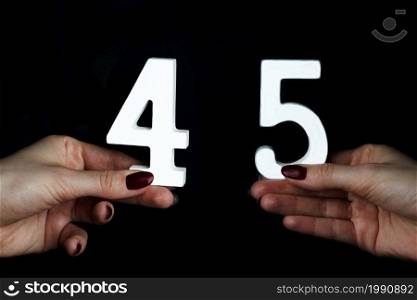 On a black background, female hand with number forty-five.. On the female palms figure forty-five.