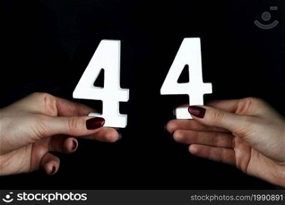 On a black background, female hand with number forty-four.. On the female palms figure forty-four.