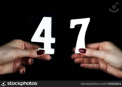 On a black background, female hand with number forty-seven.. On the female palms figure forty-seven.
