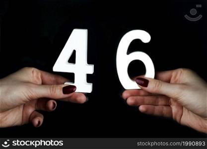 On a black background, female hand with number forty-six.. On the female palms figure forty-six.