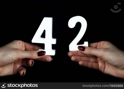 On a black background, female hand with number forty-two.. On the female palms figure forty-two.