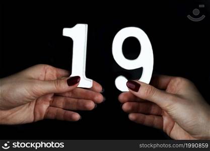 On a black background, female hand with number nineteen.. On the female palms figure nineteen.
