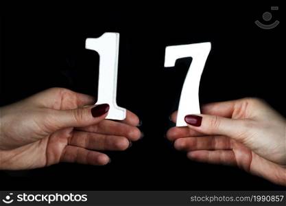 On a black background, female hand with number seventeen.. On the female palms figure seventeen.