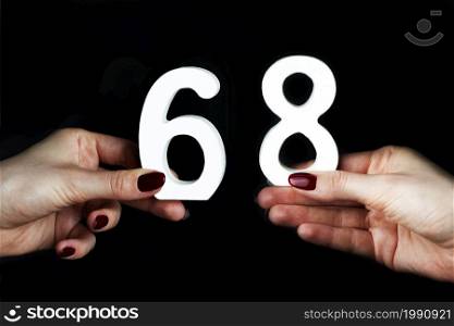 On a black background, female hand with number sixty-eight.. On the female palms figure sixty-eight.
