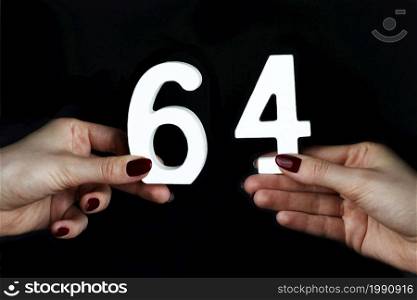 On a black background, female hand with number sixty-four.. On the female palms figure sixty-four.