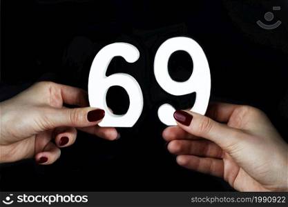 On a black background, female hand with number sixty-nine.. To female hands the number sixty-nine.
