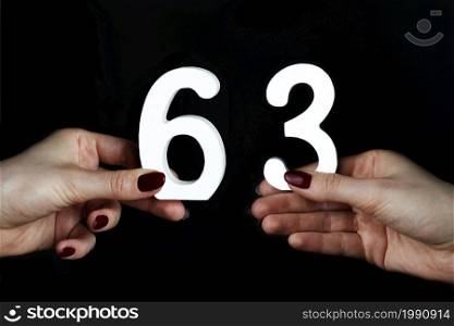 On a black background, female hand with number sixty-three.. On the female palms figure sixty-three.