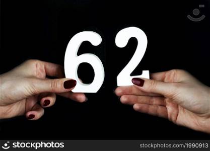 On a black background, female hand with number sixty-two.. On the female palms figure sixty-two.