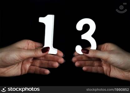On a black background, female hand with number thirteen.. To female hands the number thirteen.
