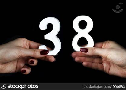 On a black background, female hand with number thirty-eight.. On the female palms figure thirty-eight.