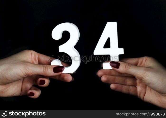 On a black background, female hand with number thirty-four.. On the female palms figure thirty-four.