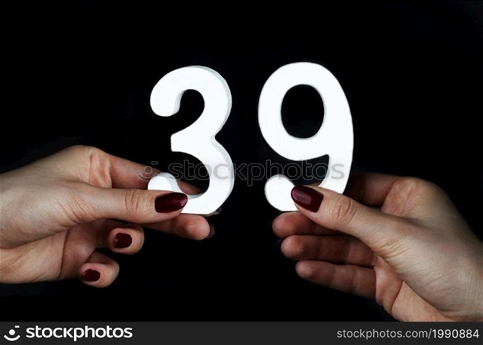 On a black background, female hand with number thirty-nine.. On the female palms figure thirty-nine.