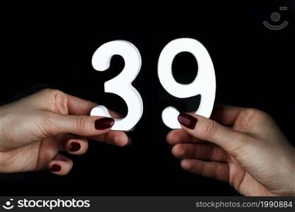 On a black background, female hand with number thirty-nine.. On the female palms figure thirty-nine.