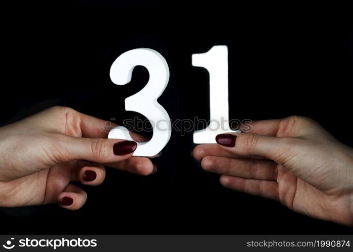 On a black background, female hand with number thirty-one.. On the female palms figure thirty-one.
