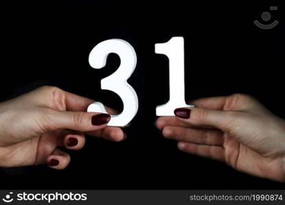 On a black background, female hand with number thirty-one.. On the female palms figure thirty-one.