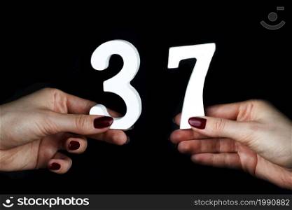 On a black background, female hand with number thirty-seven.. On the female palms figure thirty-seven.