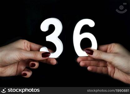 On a black background, female hand with number thirty-six.. On the female palms figure thirty-six.