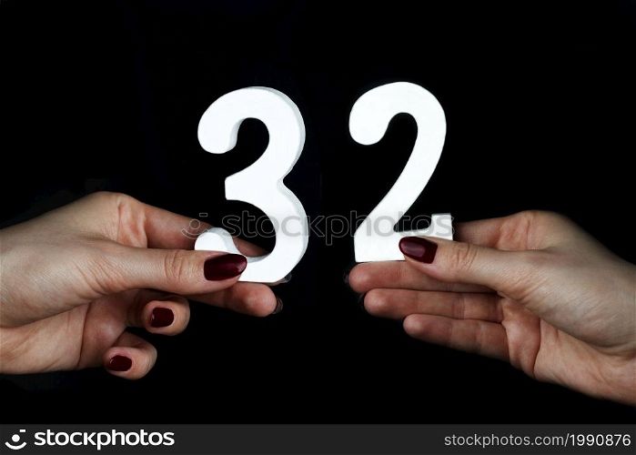 On a black background, female hand with number thirty-two.. On the female palms figure thirty-two.