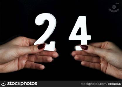 On a black background, female hand with number twenty-four.. On the female palms figure twenty-four.