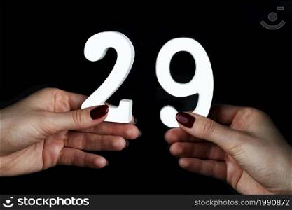 On a black background, female hand with number twenty-nine.. On the female palms figure twenty-nine.