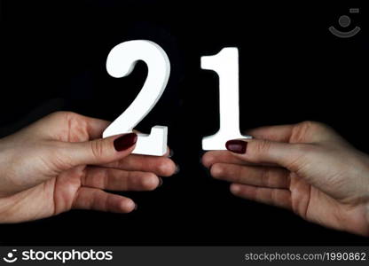 On a black background, female hand with number twenty-one.. On the female palms figure twenty-one.