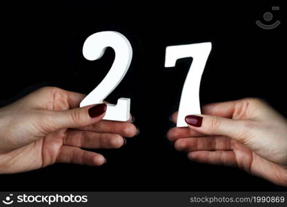 On a black background, female hand with number twenty-seven.. On the female palms figure twenty-seven.