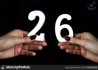 On a black background, female hand with number twenty-six.. On the female palms figure twenty-six.
