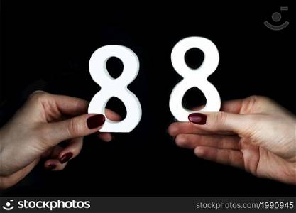 On a black background, female hand with numbers eighty-eight.. To female hands the figure of eighty-eight.
