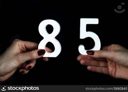 On a black background, female hand with numbers eighty-five.. To female hands the figure of eighty-five.
