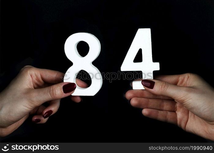 On a black background, female hand with numbers eighty-four.. To female hands the figure of eighty-four.
