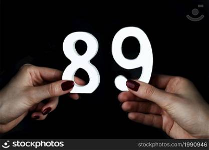 On a black background, female hand with numbers eighty-nine.. To female hands the figure of eighty-nine.