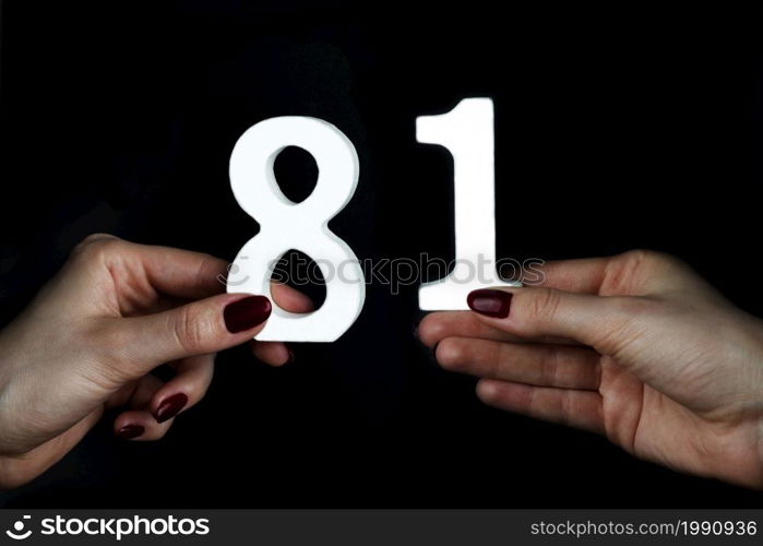 On a black background, female hand with numbers eighty-one.. To female hands the figure of eighty-one.