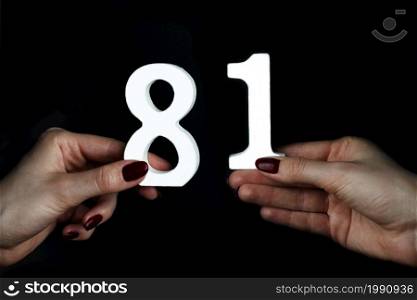 On a black background, female hand with numbers eighty-one.. To female hands the figure of eighty-one.