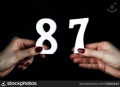 On a black background, female hand with numbers eighty-seven.. To female hands the figure of eighty-seven.
