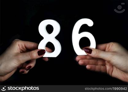 On a black background, female hand with numbers eighty-six.. To female hands the figure of eighty-six.