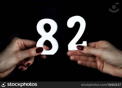 On a black background, female hand with numbers eighty-two.. To female hands the figure of eighty-two.