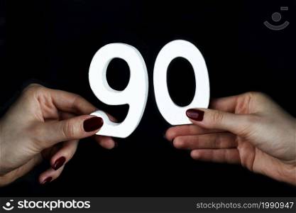 On a black background, female hand with numbers ninety.. On the female palms figure ninety.