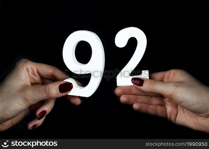 On a black background, female hand with numbers ninety-two.. To female hands the figure of ninety-two.